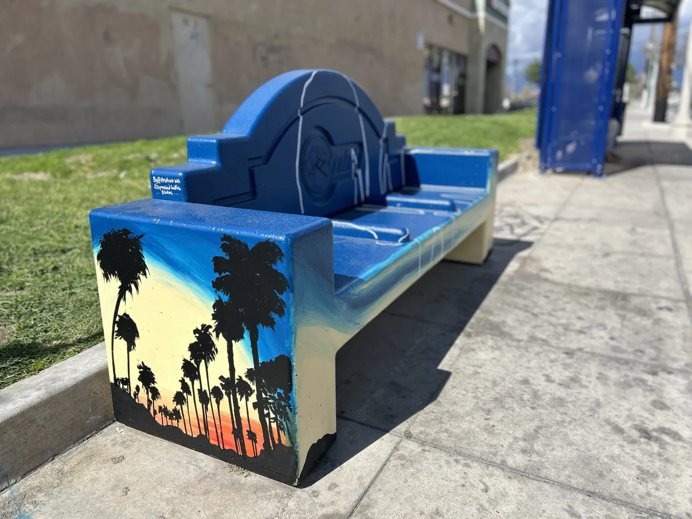 Public bench painted blue with a palm tree sunset on its side