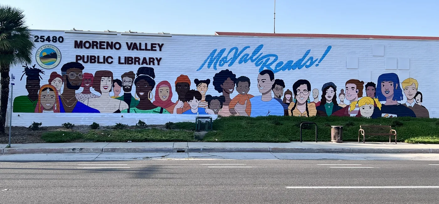 Long exterior mural of diverse faces on the Moreno Valley Public Library with the words MoVal Reads