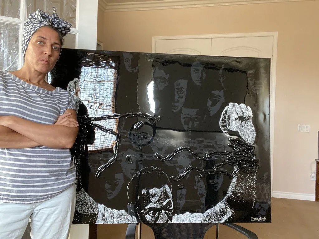 Maryam standing beside a glossy black panel of faces and a raised fist in chain and epoxy