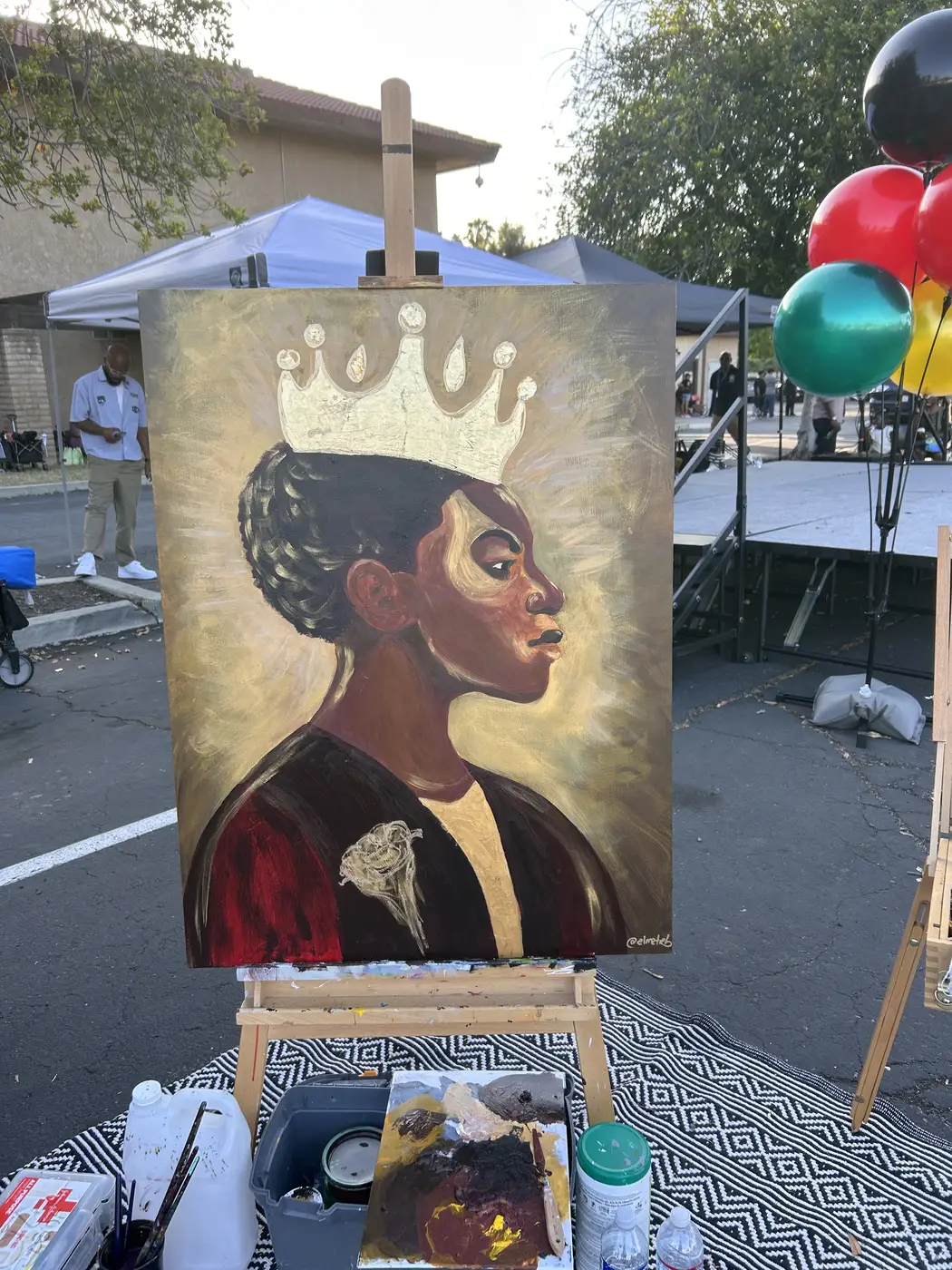 Profile portrait of a young Black girl wearing a gold crown, on an easel at an outdoor Black History Month event