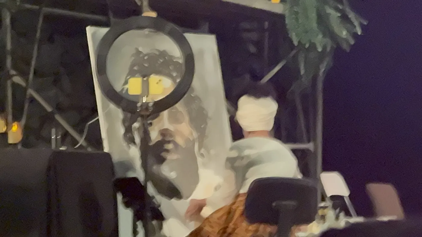Maryam painting the portrait on stage under a ring light