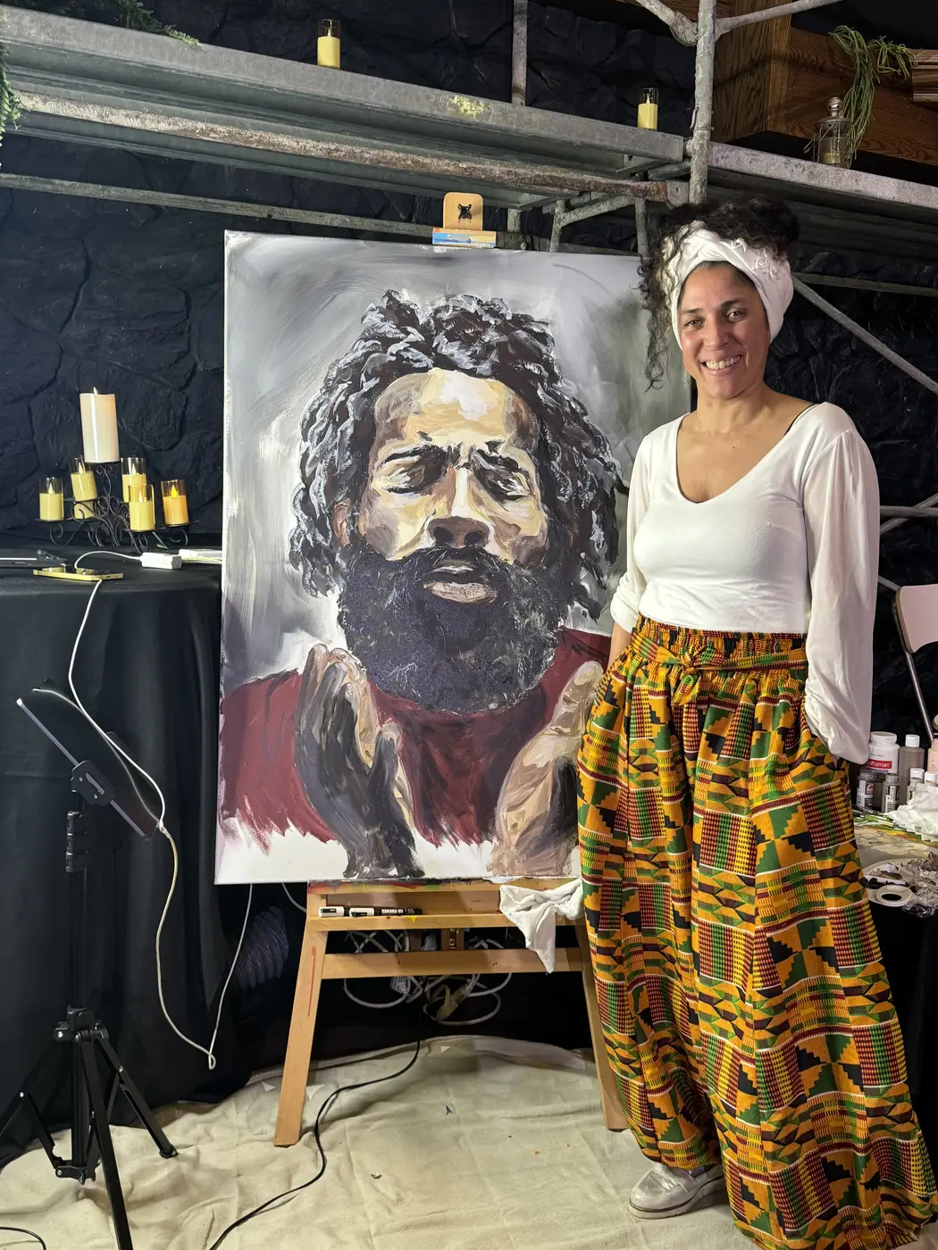 Maryam standing beside her black and white portrait of a bearded man, painted live at Mt. Rubidoux church