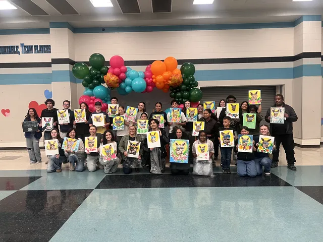 A large group in front of balloons, each person holding up a finished painting