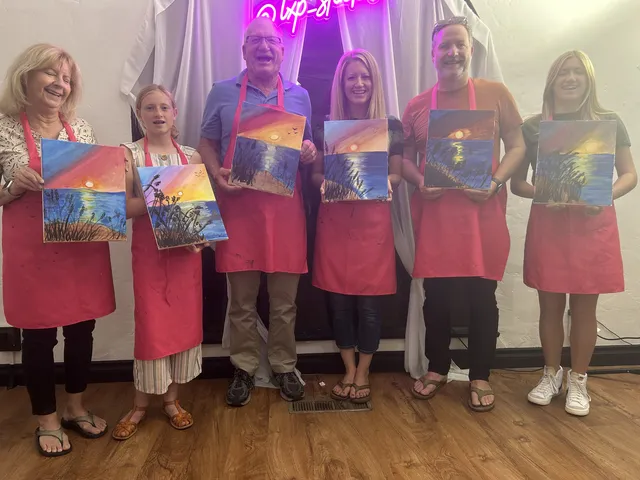 Guests in red aprons holding up their sunset paintings