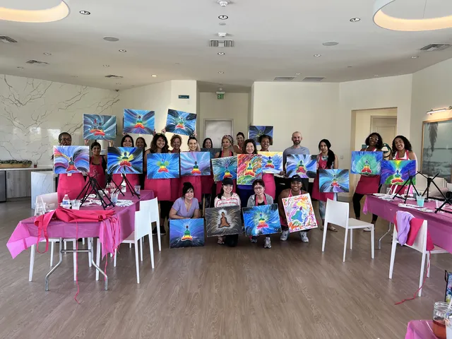 A large group in a room with pink tablecloths holding up their paintings