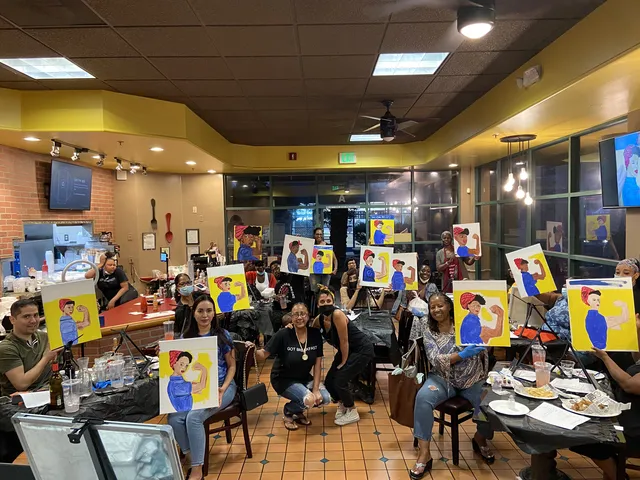 A packed restaurant paint party with guests holding up their canvases