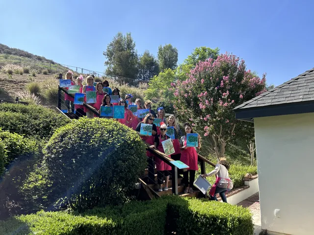 A paint party group posing on a hillside with their paintings