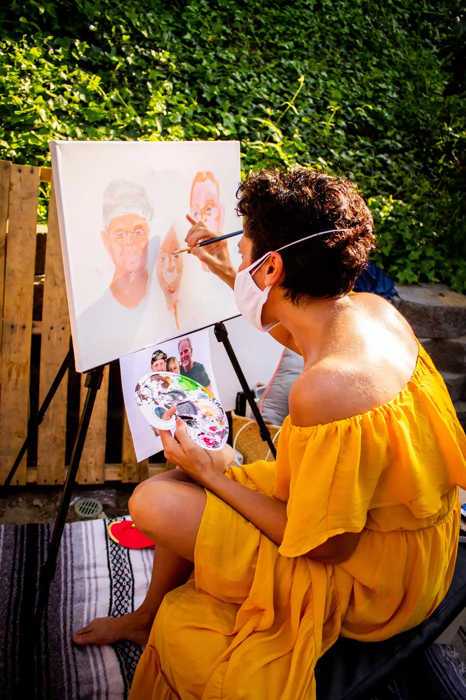 Maryam in a yellow dress painting a portrait of the birthday guests on an easel
