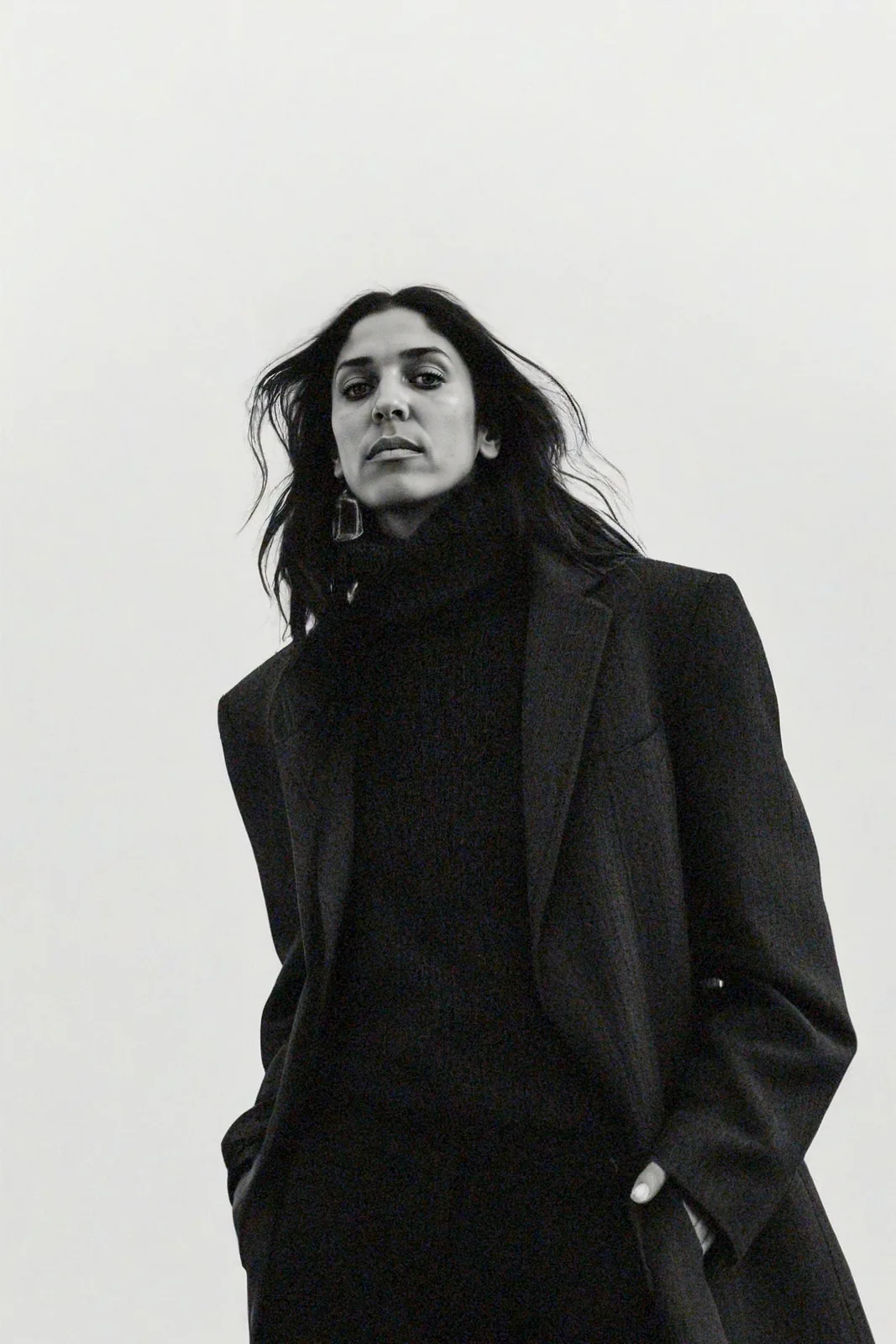 Dr. Maryam Trebeau, artist, photographed in a black coat against a pale wall