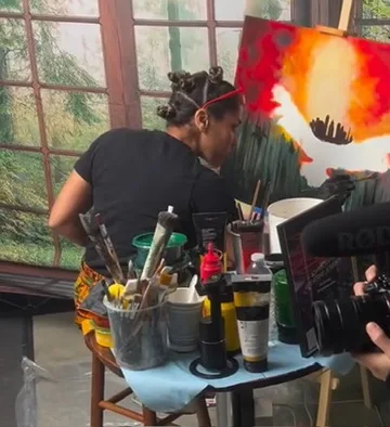 Maryam in red glasses painting an eagle rising from flames at a live radio fundraiser